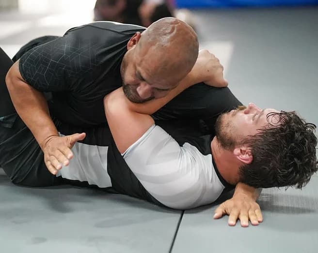 Two athletes in rash guards grappling on the mat during a No-Gi class.